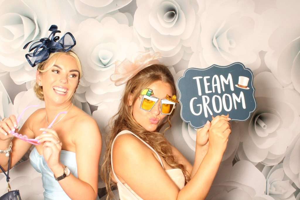 Two guests posing with novelty glasses and a Team Groom sign at a photo booth